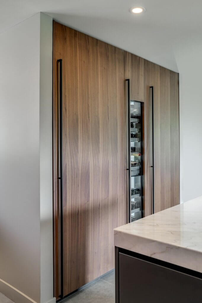 Contemporary kitchen design featuring sleek wood-paneled cabinetry with integrated handles and a built-in wine storage area, paired with a marble countertop in the foreground.