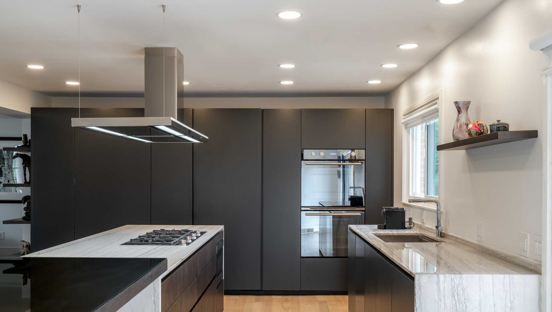 Architectural redesign of a modern kitchen in Amberley Village featuring sleek matte cabinetry, quartzite countertops, a waterfall island in statuary quartzite with olmo bruno wood, and an Italian ceiling-mounted range hood. Natural light and minimalist design highlight the fusion of art and function.