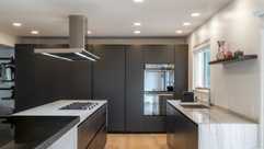 Architectural redesign of a modern kitchen in Amberley Village featuring sleek matte cabinetry, quartzite countertops, a waterfall island in statuary quartzite with olmo bruno wood, and an Italian ceiling-mounted range hood. Natural light and minimalist design highlight the fusion of art and function.