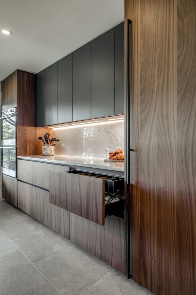 Modern minimalist kitchen design showcasing streamlined wood cabinetry with integrated handles, sleek matte upper cabinets, under-cabinet lighting, and a concealed wine storage drawer.