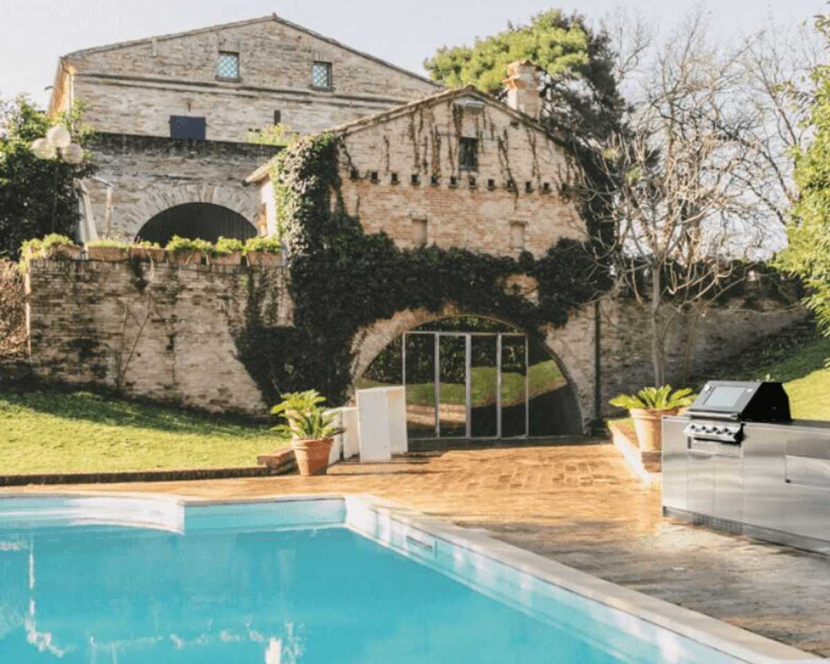 Stainless steel Italian outdoor kitchen beside a pool with stone architecture in the background. Stainless steel Italian outdoor kitchen beside a pool with stone architecture in the background.